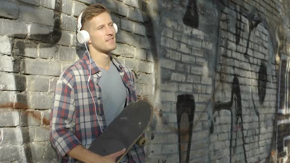 Handsome male with skateboard listening favorite music on smartphone, hobby