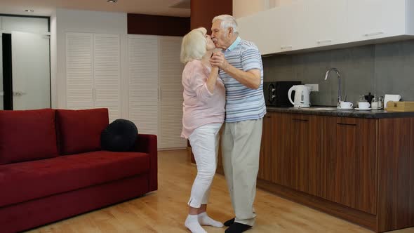 Happy Mature Senior Couple Dancing Laughing in Kitchen at Home, Celebrating Anniversary, Having Fun