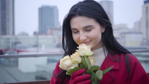 Close-up Portrait of Young Caucasian Woman with Black Hair Smelling Yellow Roses and Smiling