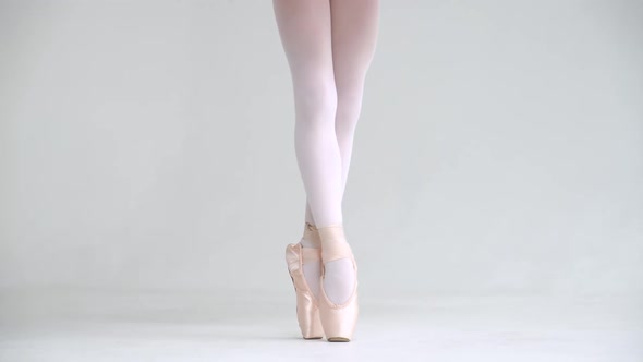 Little Girl in a White Tutu Balancing in Pointe Shoes View of the Legs White Background