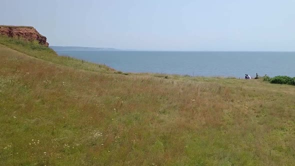 STATIC CROP, Aerial, flying over a grassy bluff toward red sandstone cliffs and the ocean