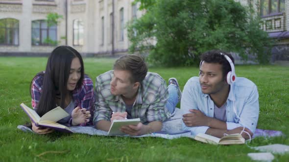 Mixed-Race Fellows Having Rest on Lawn on College Campus, Enjoying Hobbies