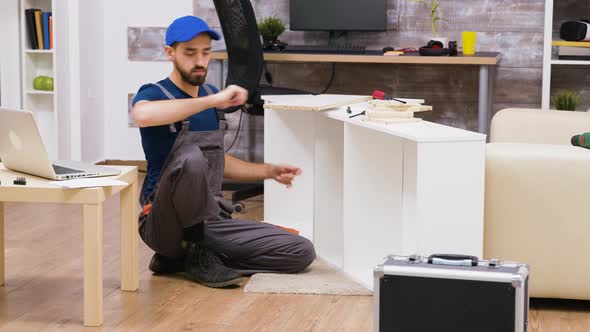 Professional Worker in Overalls Consults Furniture Assembly Instructons