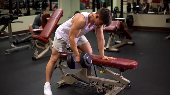 Front side shot of young bodybuilder doing one arm dumbbell rows using a bench.