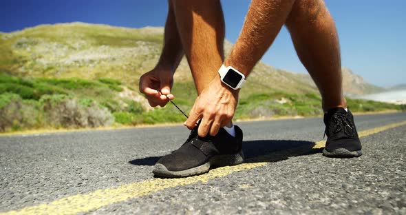 Triathlete man tying his shoe lace in the countryside road