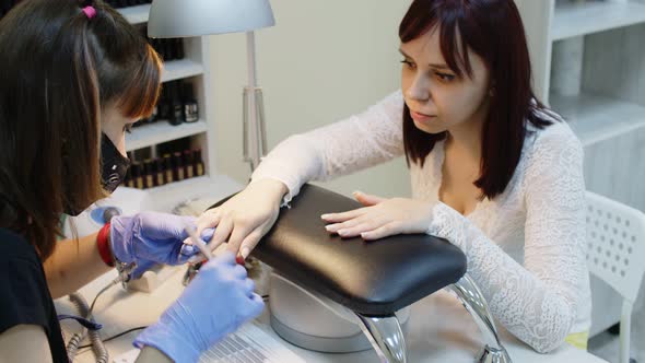 Unrecognizable Person in Gloves Saws Nails of Young Woman in Salon