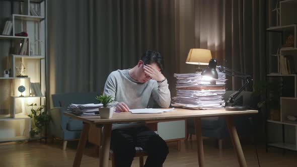 Tired Asian Man Shaking His Head While Working Hard With Documents At The Home