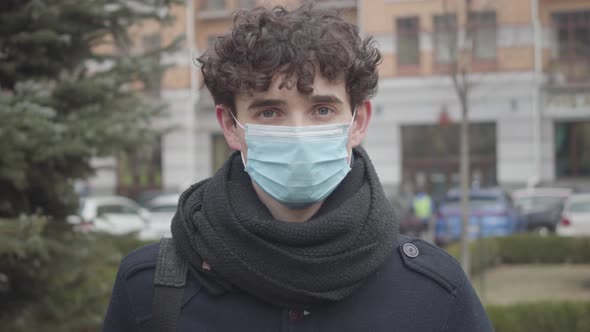 Close-up Portrait of Young Caucasian Boy in Face Mask Posing on City Street. Handsome Brunette Guy