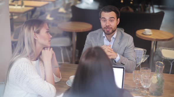 group of people sits at a wooden table with a laptop near a window and tells their business ideas.