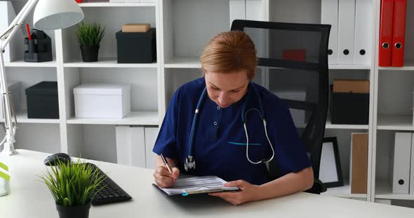 Doctor in Office Filling Form and Looking at Camera