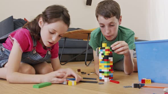 Girl and a boy playing and constructing with toy bricks on the living room floor