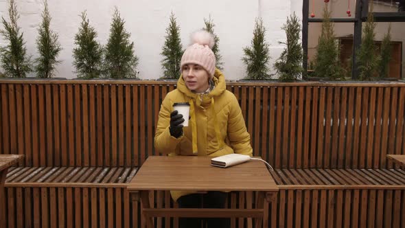 Portrait of a Young Girl in a Coat Sitting on the Street in the Empty Cafe