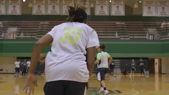 Woman basketball player runs down court dribbling ball towards basket with players watching. Camera