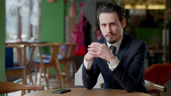 Middle Shot Portrait of Confident Bearded Man with Mustache Sitting in Cafe Looking at Camera