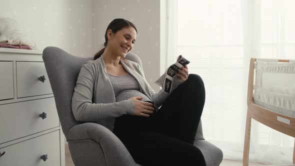 Mid shot video of caucasian woman in advanced pregnancy browsing ultrasound scan in baby's room.