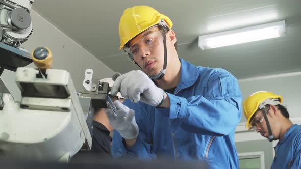 Asian mechanical technicians wear hardhat and glasses workers working on milling machine in factory.