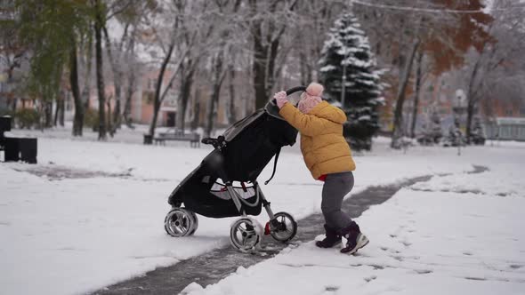 Toddler Child Pushing Stroller with Sibling in It. Winter Snowy Day. Christmas Time