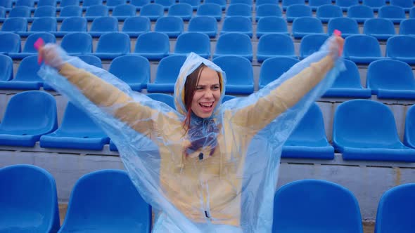 Young Woman in Raincoat Sitting on Stadium Bleachers Alone Rooting for Favorite Sports Team