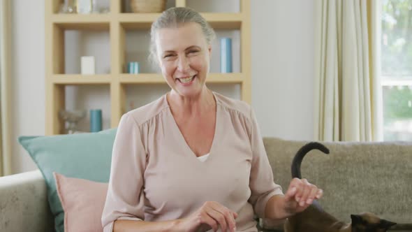 Portrait of happy senior caucasian woman sitting and making video call with cat in living room