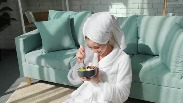 Happy Lady Sitting Near Sofa After Shower and Eating Granola with Yogurt and Fruit