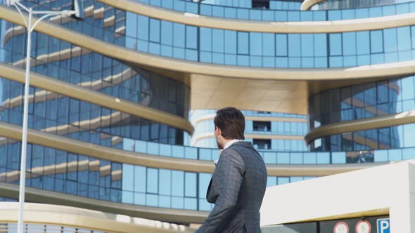 Young Businessman in a Suit Standing Near a Glass Skyscraper and Talking on a Mobile Phone, Top
