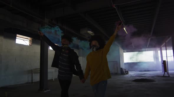 Mixed race man and woman holding blue and purple flares walking through an empty building