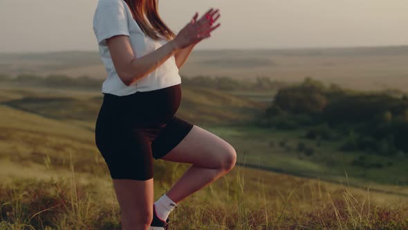 Pregnant woman stands in yoga pose outdoor on hill, side view. Pregnant woman