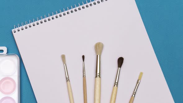 Brushes and Sketchbook on a Blue Background