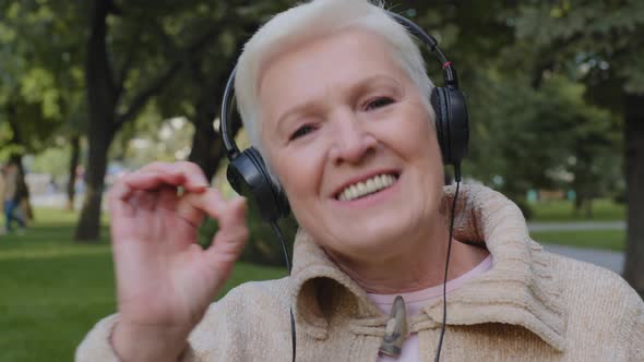 Happy Satisfied Elderly Lady of Retirement Age Wearing Earphone Outdoors Listening Favorite Music