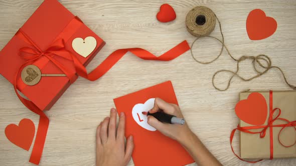 Hand Writing Love Word on Greeting Card Lying on Table With Craft Gift Boxes