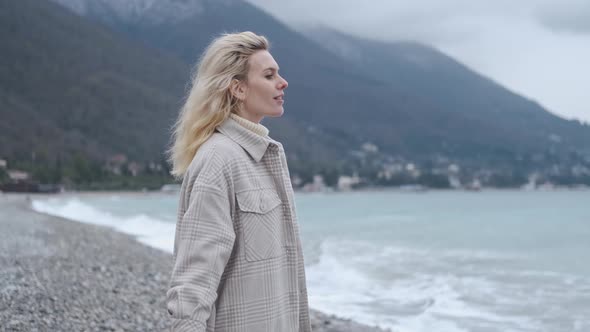 woman breathes cold air on the beach among the mountains