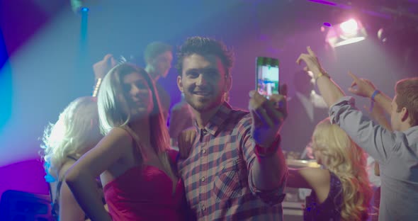 Friends taking self photograph with mobile phone while enjoying music in nightclub