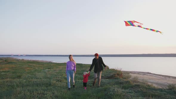 Happy Family Walking with Flying Kite on Field Near Seashore During Sunset Slow Motion