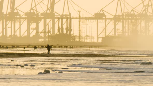 Silhouette of industrial container harbor with sandy beach and people in foreground