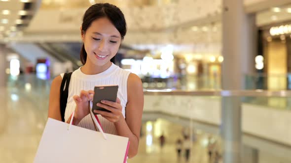 Woman Using Cellphone and Holding Shopping Bags in Shopping Center