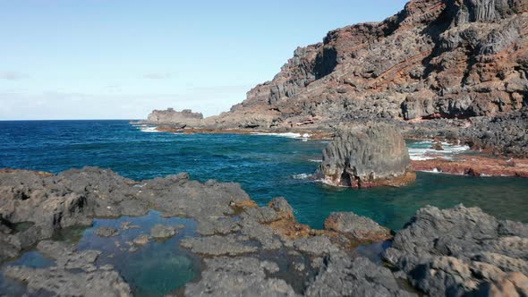 Aerial dolly over Atlantic ocean coast with volcanic relief in sunny