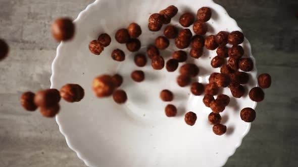 Dry Breakfast Consisting of Chocolate Cornflakes is Falling in Slowmo Into a White Dish