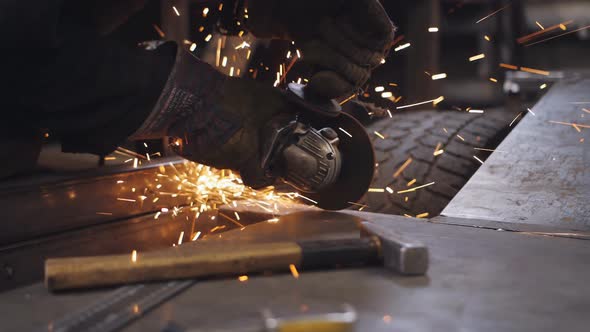 A Mechanic in an Auto Repair Shop with a Grinder Cuts Off a Metal Part Near the Wheel of a Car