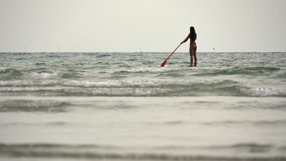 Woman Standing On Paddleboard And Rowing Out To Sea