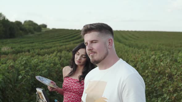 Creative Artist Looks Straight and Smiles When His Girl Painting in Field