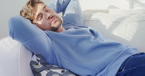 Young man sleeping on sofa at home on a sunny day 4K