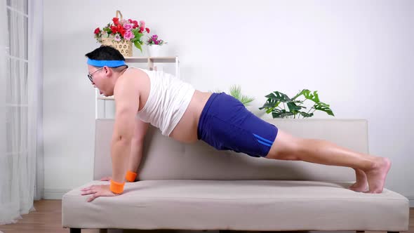 Funny fat Asian man trying harder exercise workout on sofa in living room by push up