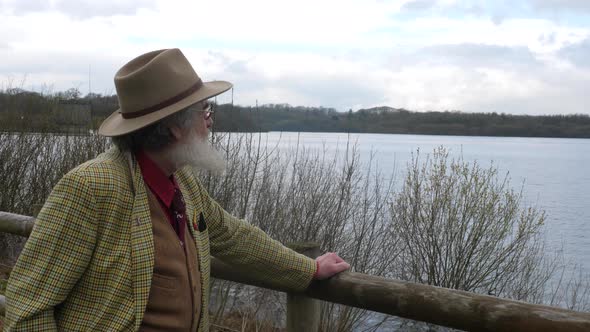 An elderly man looking out over the lake while holding onto fence