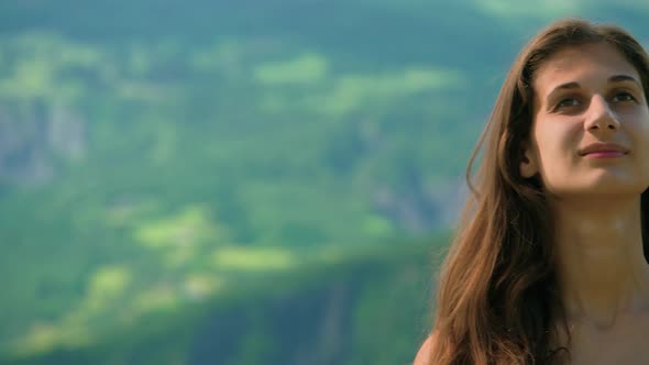 A woman standing in a field with mountains in the distance looking happy and smiling with laughter.