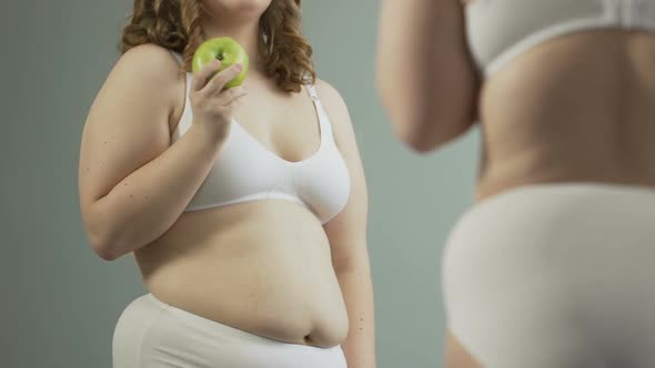 Overweight Woman in Underwear Admiring Her Body in Mirror and Eating Green Apple