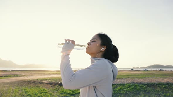 Young Asian woman running drink water after workout outdoors in the mountains.