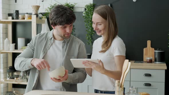 Young Married Couple Uses a Digital Tablet and Smiles While Cooking in the Kitchen at Home