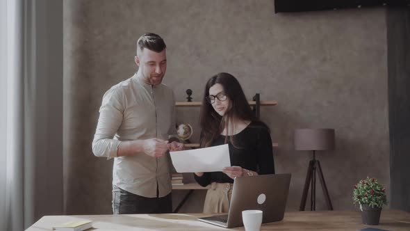 Male Coworker Showing Document with Project Results Talking To Caucasian Female Colleague