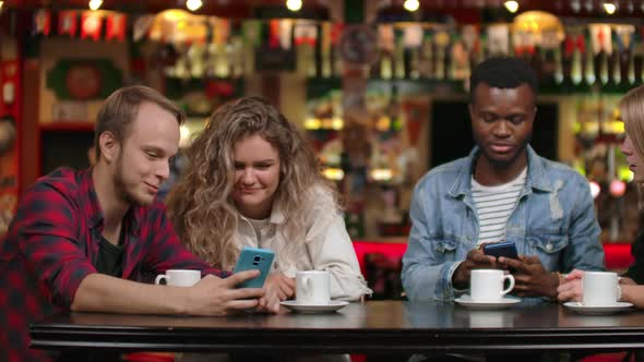 Group of Friends at a Bar Drinking Coffee and Discussing While Looking at the Screen of a Smartphone