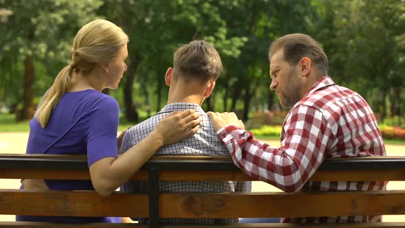 Caring Mother and Dad Supporting Sad Teen Son Sitting on Bench in Park, Crisis